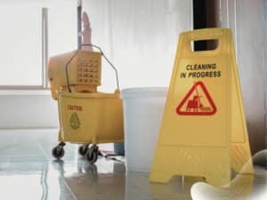 Close up yellow warning sign with message Cleaning in progress with cleaning trolley. Concept of slip and fall claims.